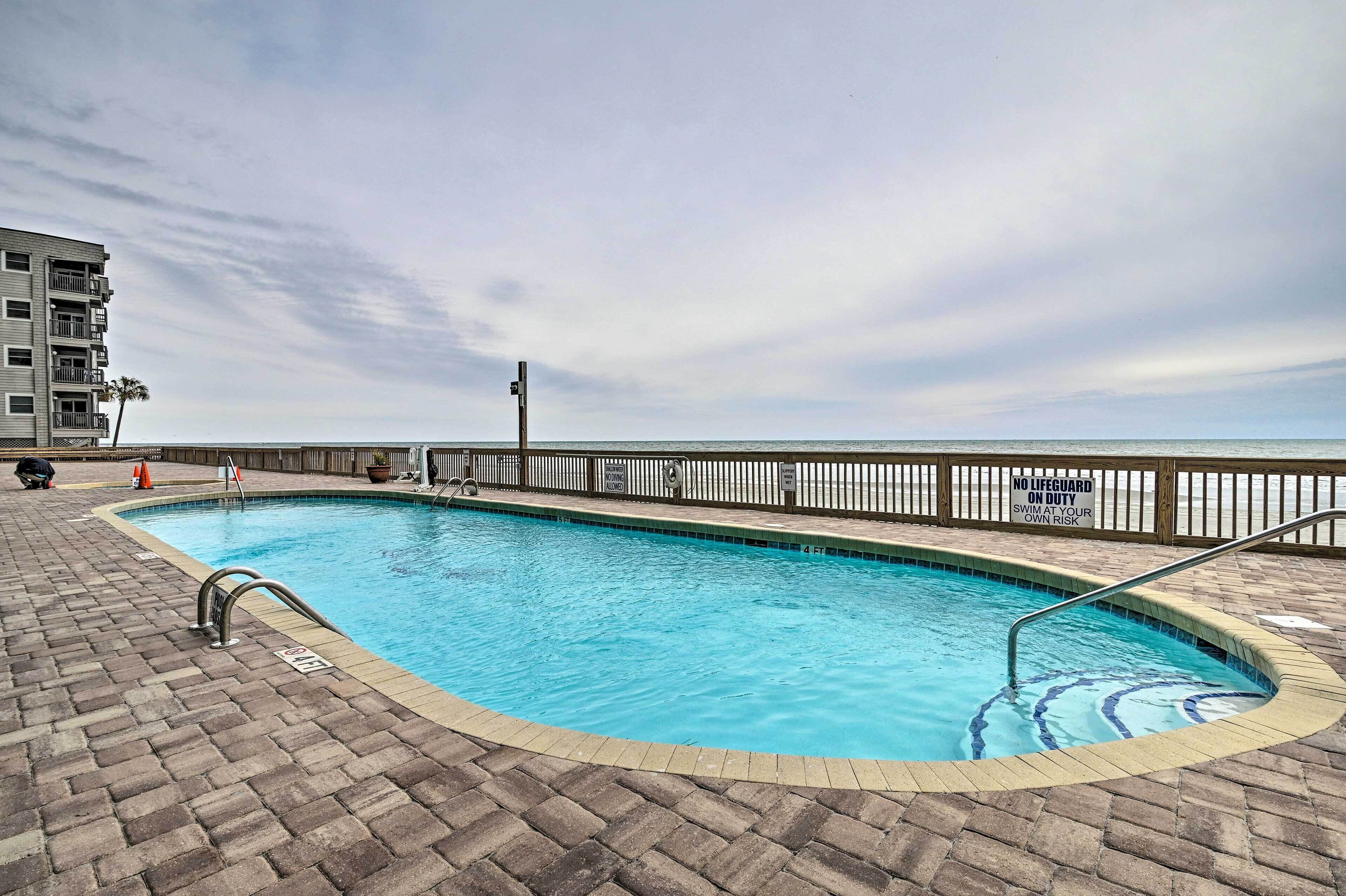 A swimming pool with a brick deck, a lifeguard stand, and a view of the ocean.