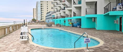 Un espace piscine avec un panneau indiquant « PISCINE FERMÉE », un poste de surveillance pour les sauveteurs et une vue sur l’océan.