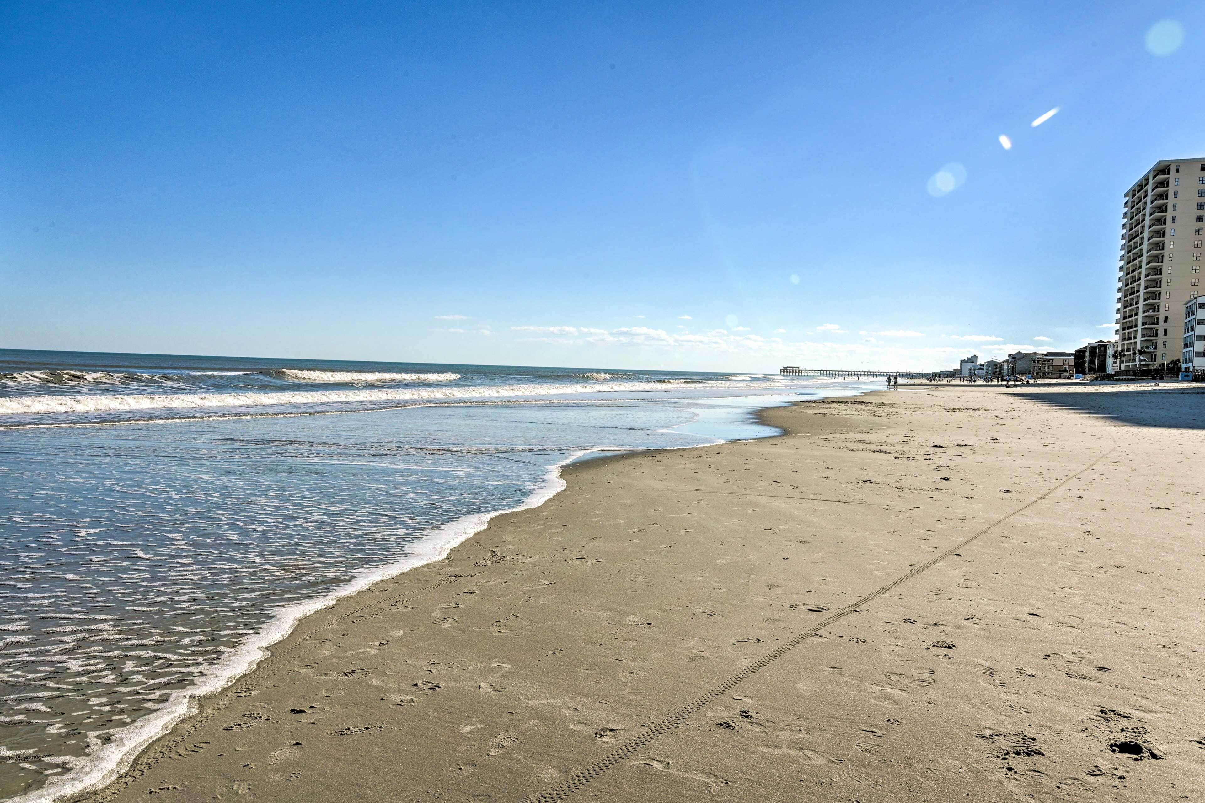 A beach with a clear sky, waves, and a building on the right.