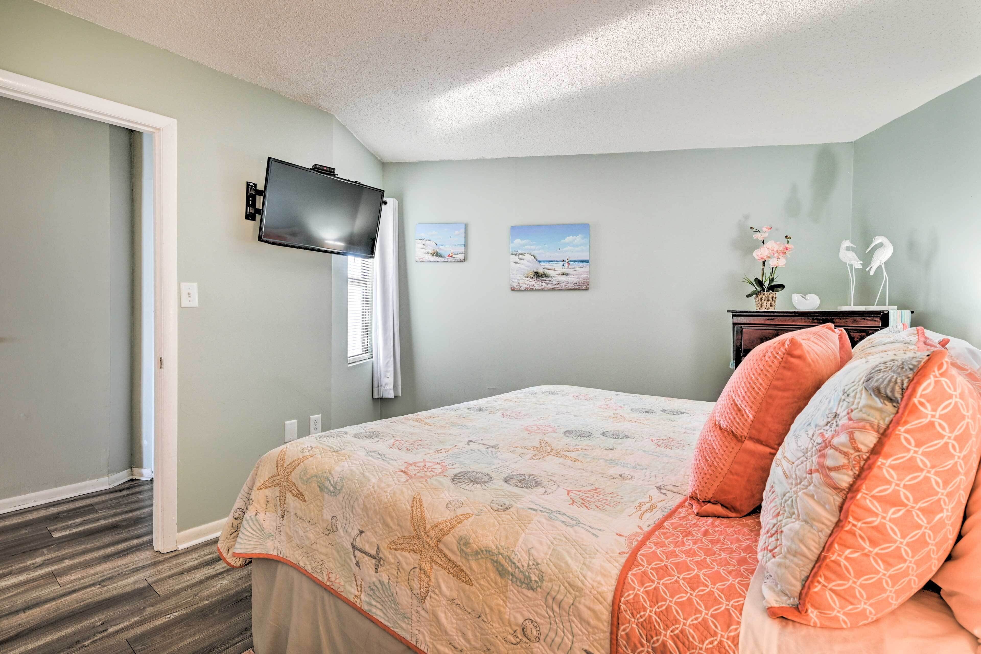 A bedroom with a bed, a television mounted on the wall, and two framed pictures on the wall.