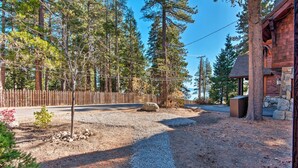 Une cabane rustique avec une allée en gravier, entourée de grands pins et d’une clôture en bois.