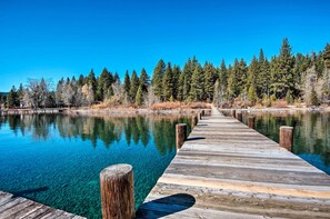 A wooden pier extending into a clear blue lake, surrounded by dense forest.