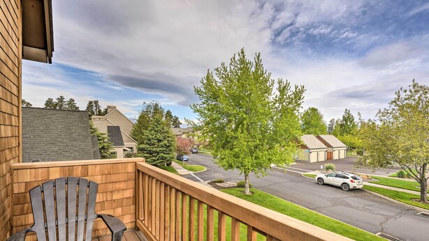 A wooden deck with a black Adirondack chair, a view of a suburban street with houses and a white car parked on the road.
