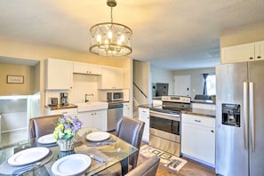 A modern kitchen with stainless steel appliances, white cabinetry, and a glass dining table set for four.