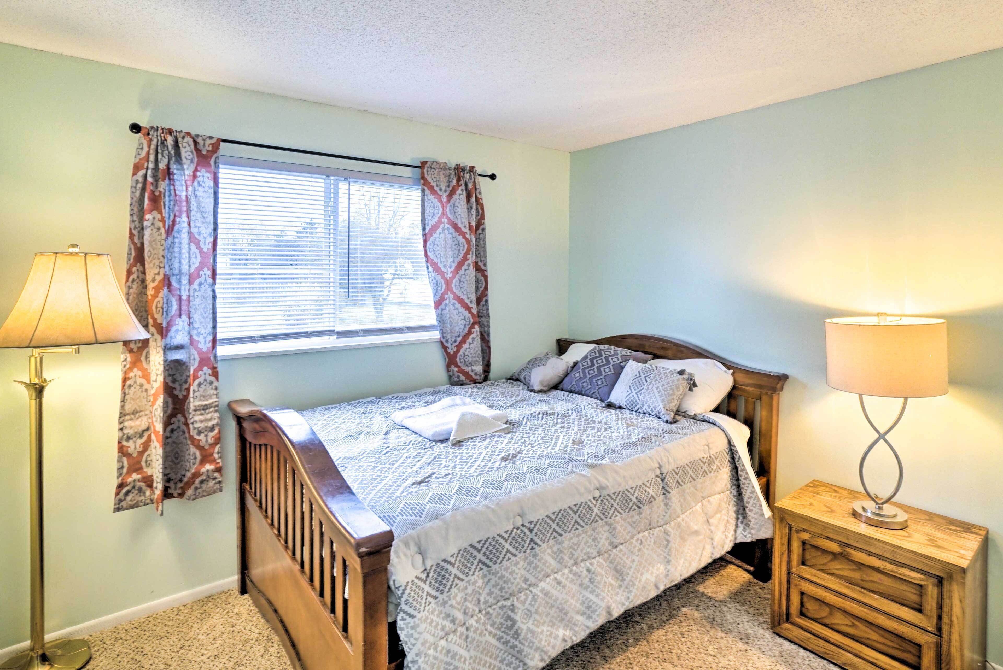 A bedroom with a bed, a nightstand, a lamp, and a window with curtains.