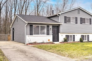 A two-story house with a grey siding exterior, a black front door, and a small front yard with a sidewalk.