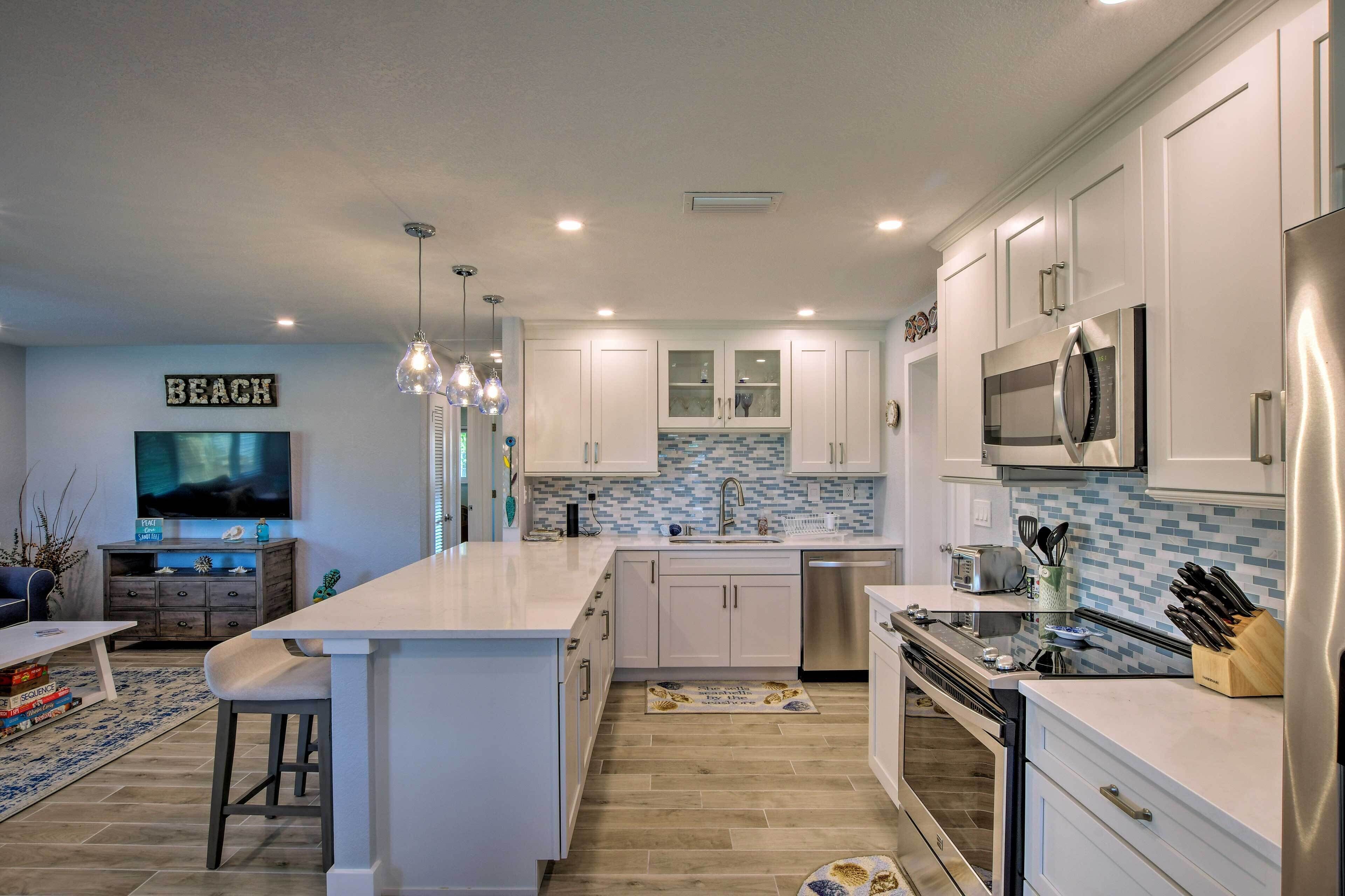 A modern kitchen with white cabinets, a large island, stainless steel appliances, and a tiled backsplash.