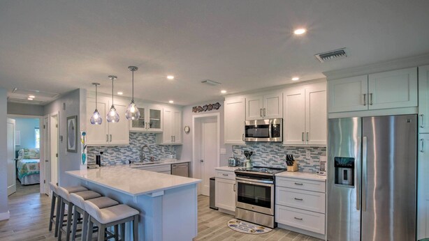 Una cocina moderna con armarios blancos, electrodomésticos de acero inoxidable y una isla central con taburetes de bar.