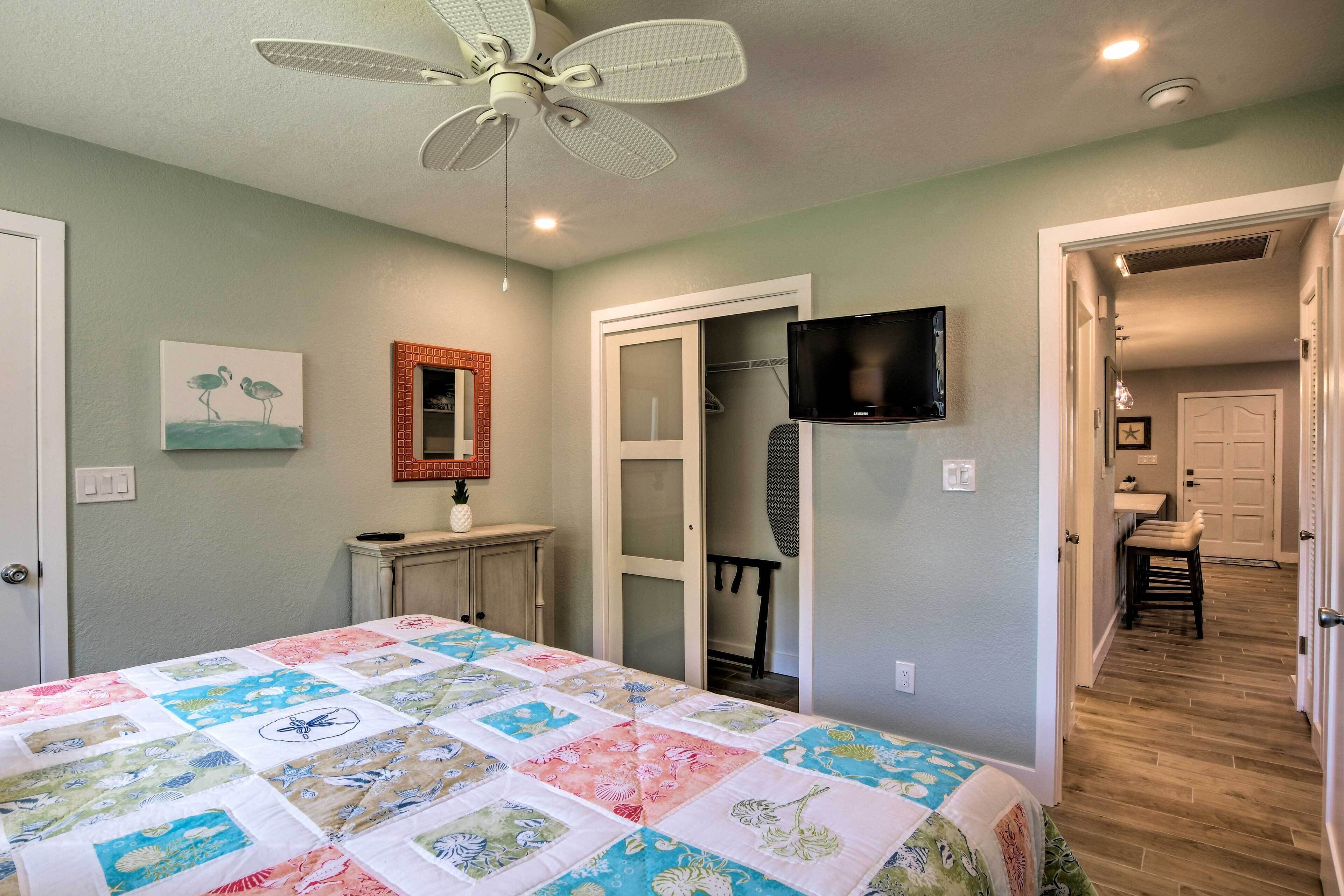 A bedroom with a bed, a ceiling fan, a TV, and a door leading to a bathroom.