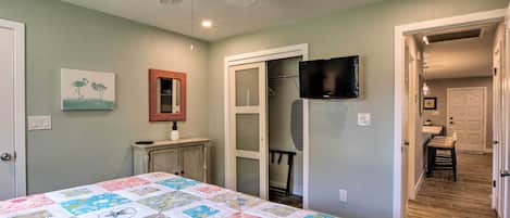 A bedroom with a bed, a ceiling fan, a TV, and a door leading to a bathroom.