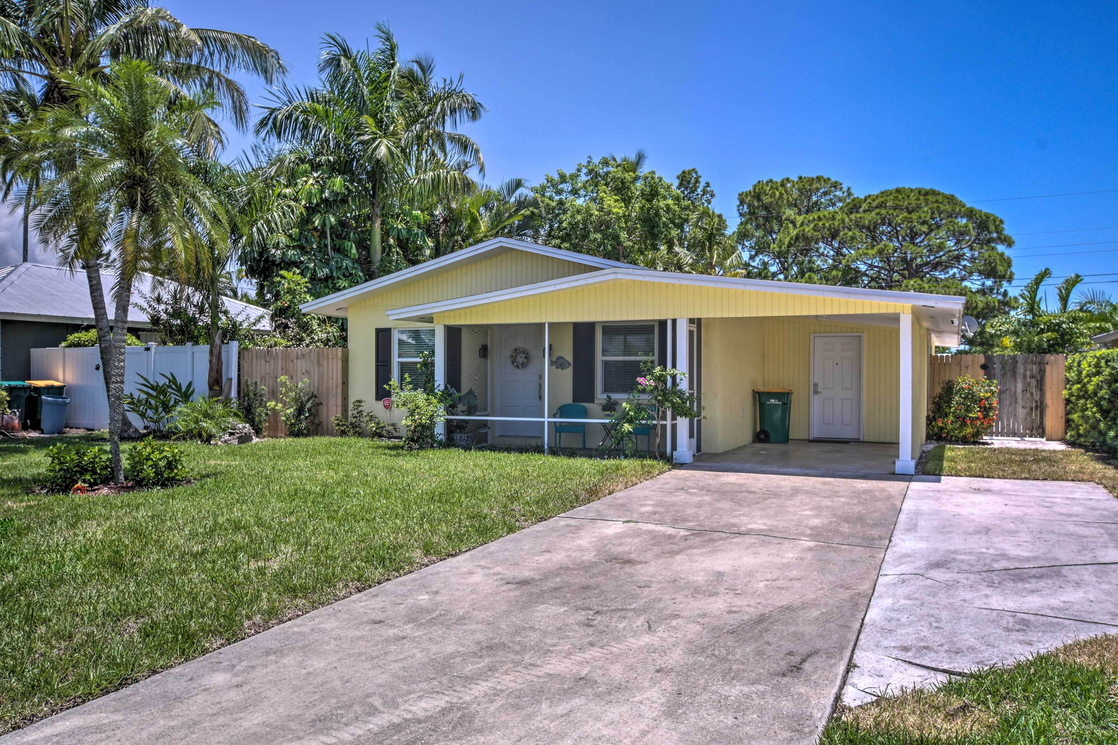 A single-story house with a yellow exterior, a covered porch, and a front yard with grass and palm trees.