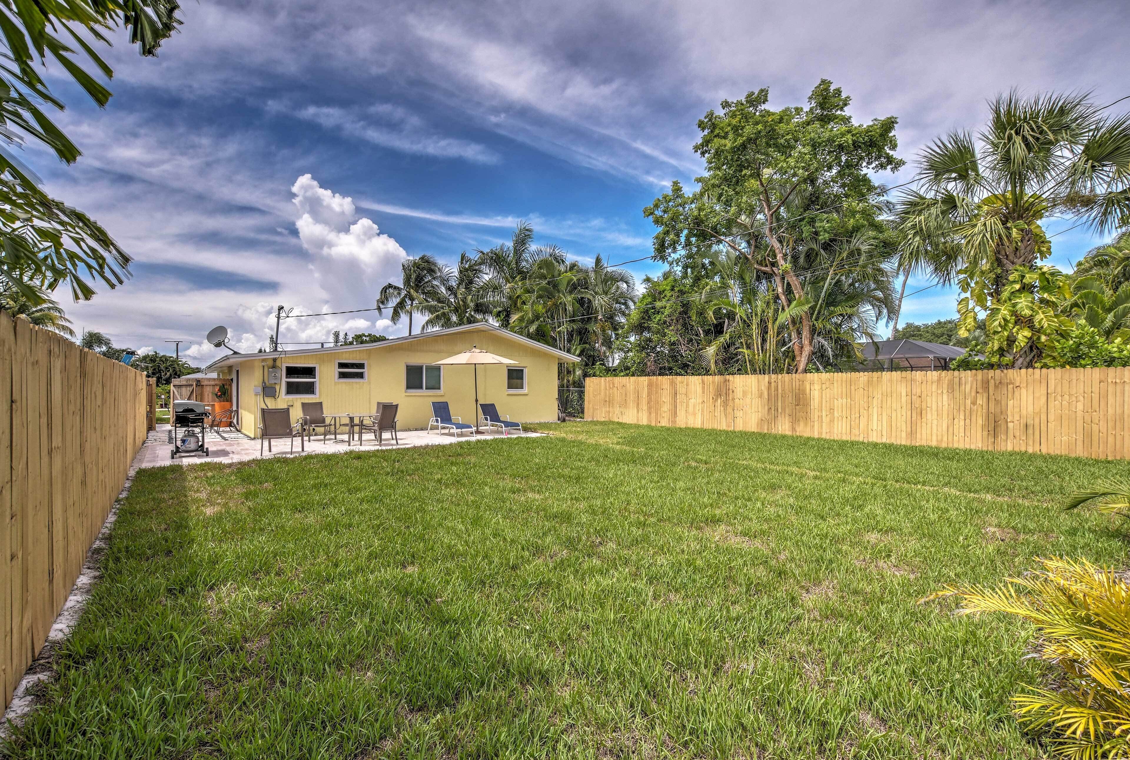 A backyard with a yellow house, a wooden fence, and a lawn.
