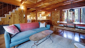 A cozy cabin interior with a wooden staircase, a blue sofa, a dining table, and a view of the outdoors. - Boutique + Artsy Log Cabin in North Lake Tahoe! (Kings Beach)