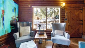 A cozy log cabin interior with two armchairs, a coffee table, and a large window offering a view of the outside. - Boutique + Artsy Log Cabin in North Lake Tahoe! (Kings Beach)