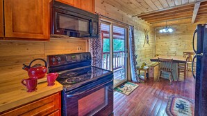 A wooden cabin kitchen with a stove, microwave, and red kettle. - Secluded Johnsburg Retreat w/ Hot Tub & Fire Pit (Johnsburg)