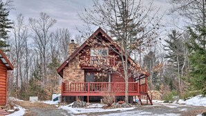 A log cabin with a wooden deck and a chimney, surrounded by trees and a gravel path. - Secluded Johnsburg Retreat w/ Hot Tub & Fire Pit (Johnsburg)