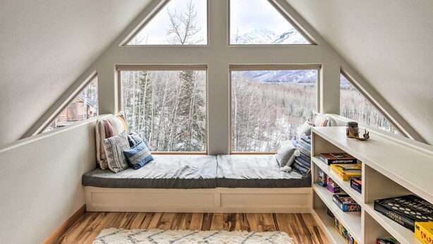 A cozy attic bedroom with a built-in window seat, wooden flooring, and a bookshelf filled with board games. - Alaskan Mountain Gem With Private Hot Tub & Gym! (Eagle River)