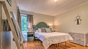 A bedroom with a bed, bedside tables, a dresser, a window with curtains, and a ladder leaning against the wall.
