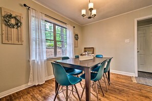 A dining area with a wooden table and teal chairs, a window with white curtains, and a chandelier. - Centrally Located Hot Springs Home w/ Deck! (Hot Springs)