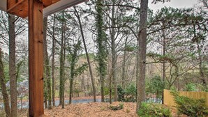 A wooden deck with a view of a forested area, a wooden fence, and a small pond.