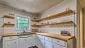 A kitchen with white cabinets, wooden countertops, and a window.