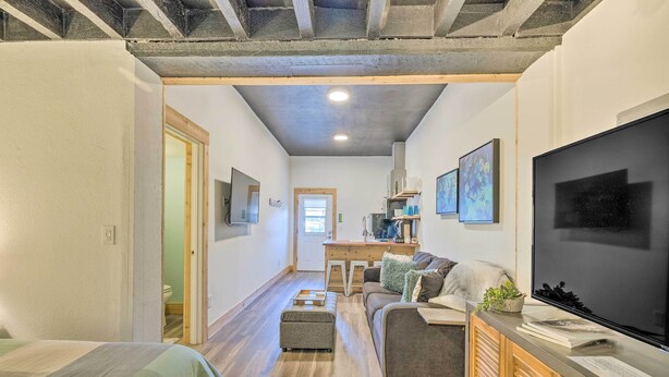Un soggiorno moderno con divano, poggiapiedi e televisore a schermo piatto. Si nota un mobile contenitore in legno e una scrivania con una sedia.