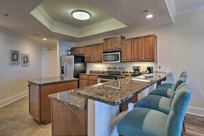 A modern kitchen with granite countertops, wooden cabinets, a built-in microwave, and a stainless steel refrigerator.