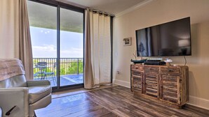 A living room with a sofa, a flat-screen TV, and a wooden cabinet. - Dauphin Island Condo w/ Pool, Balcony & Ocean View (Dauphin Island)