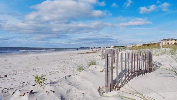 Une plage de sable avec une clôture en bois et un bâtiment en arrière-plan.