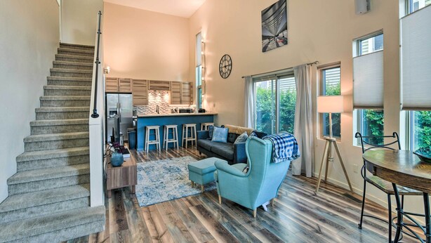 A spacious living area with a staircase, a kitchen with bar stools, a dining table, and large windows.