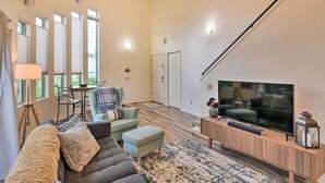 A spacious living room with a large flat-screen TV, a sofa, a dining table, and a staircase leading to another level.