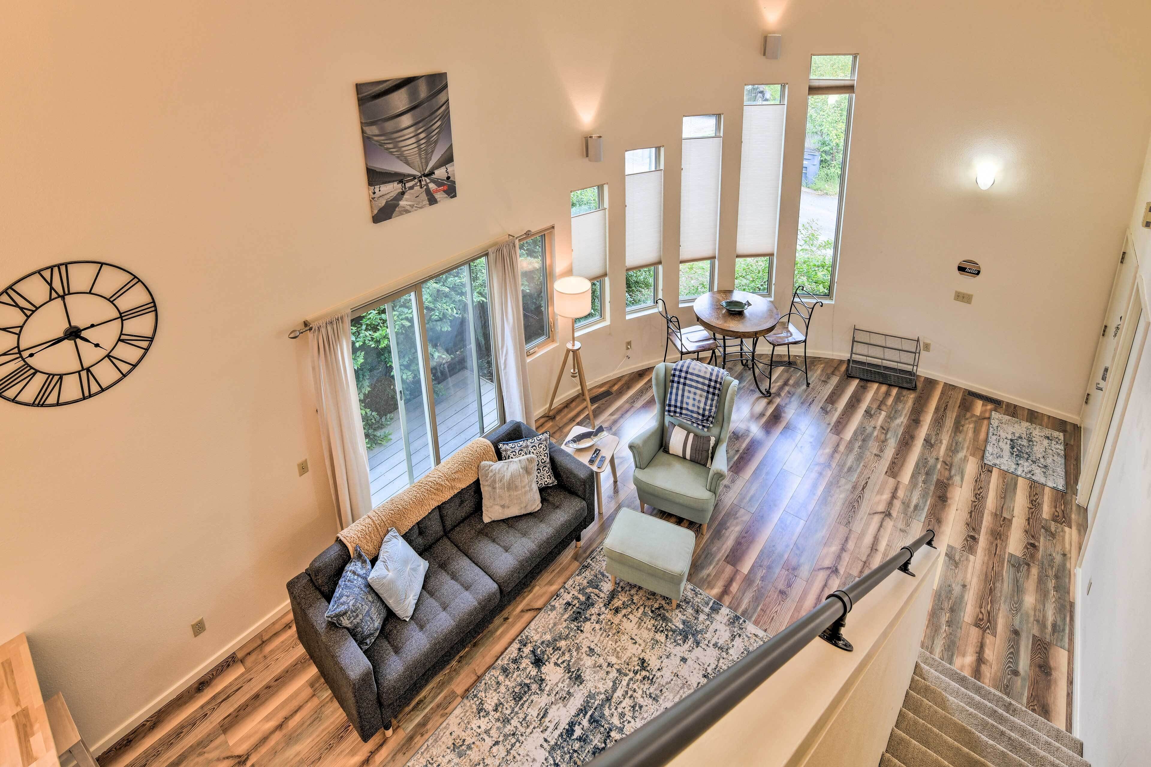 A spacious living area with a dark gray sofa, a small round table, and a view of the outdoors through large windows.