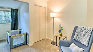A room with a playpen near a window, a lamp, a chair, and a small table with a plant.