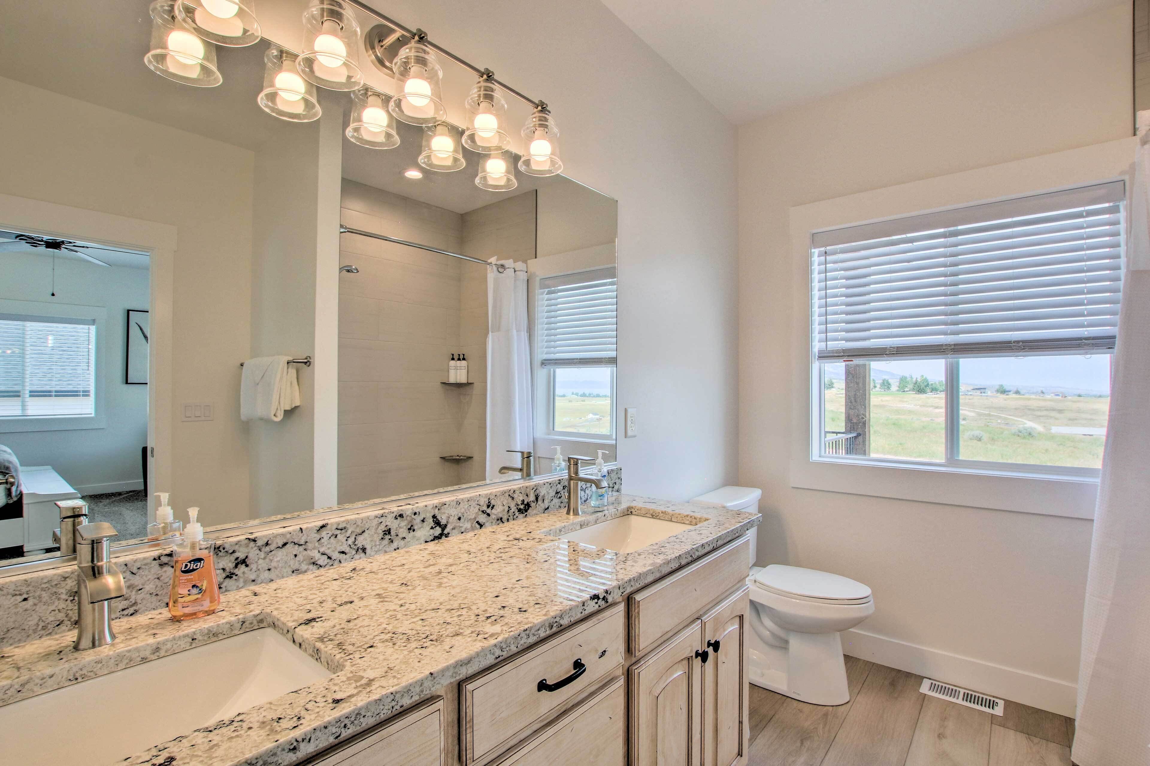 A bathroom with a granite countertop, a large mirror, a toilet, and a window with blinds.