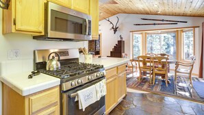 A kitchen with wooden cabinets, a stove, and a microwave. There is a dining area with chairs and a table. - 7 Mi to Northstar Resort: Tahoe Vista Family Cabin (Kings Beach)