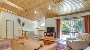 A spacious living room with a wooden ceiling, a sofa, a chair, a TV on a stand, and a large window with curtains. - 7 Mi to Northstar Resort: Tahoe Vista Family Cabin (Kings Beach)