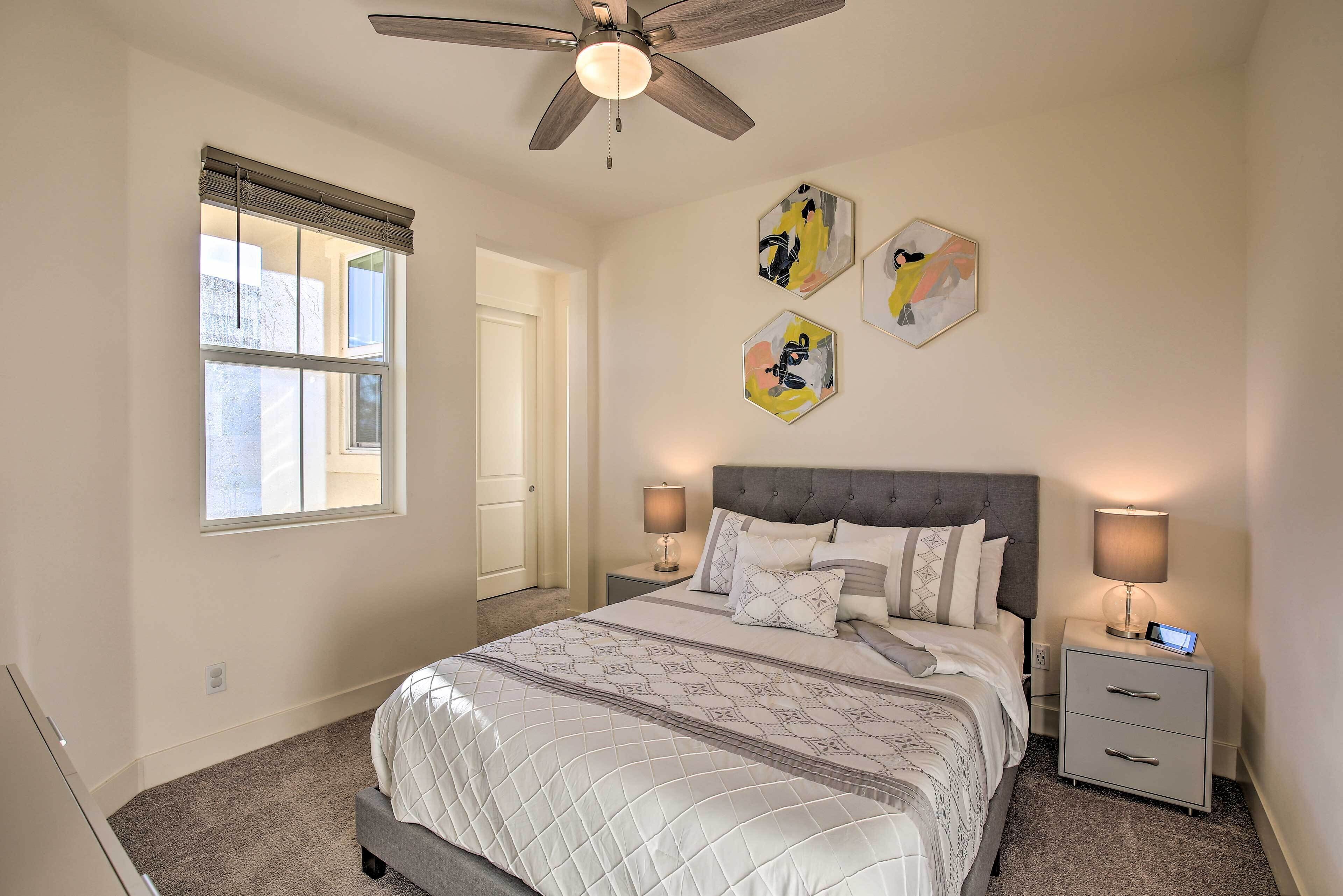 A bedroom with a bed, two bedside tables, a ceiling fan, and artwork on the wall.