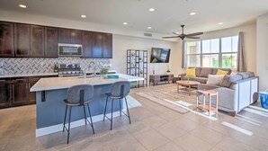 A modern kitchen with dark cabinets, a central island with bar stools, a microwave, and a TV above the island. - Lakefront Indio Villa: Private Pool & On-site Golf (Indio)