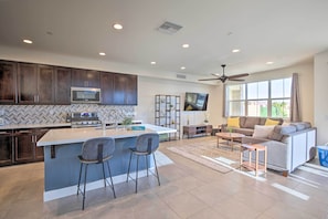 A modern kitchen with dark cabinets, a central island with bar stools, a microwave, and a TV above the island. - Lakefront Indio Villa: Private Pool & On-site Golf (Indio)