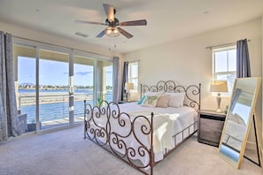 A bedroom with a bed, a ceiling fan, a nightstand, a lamp, a mirror, and a view of the water. - Lakefront Indio Villa: Private Pool & On-site Golf (Indio)