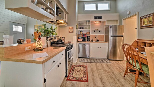 A compact kitchen with a wooden countertop, built-in shelves, a refrigerator, and a dining area with a chair.