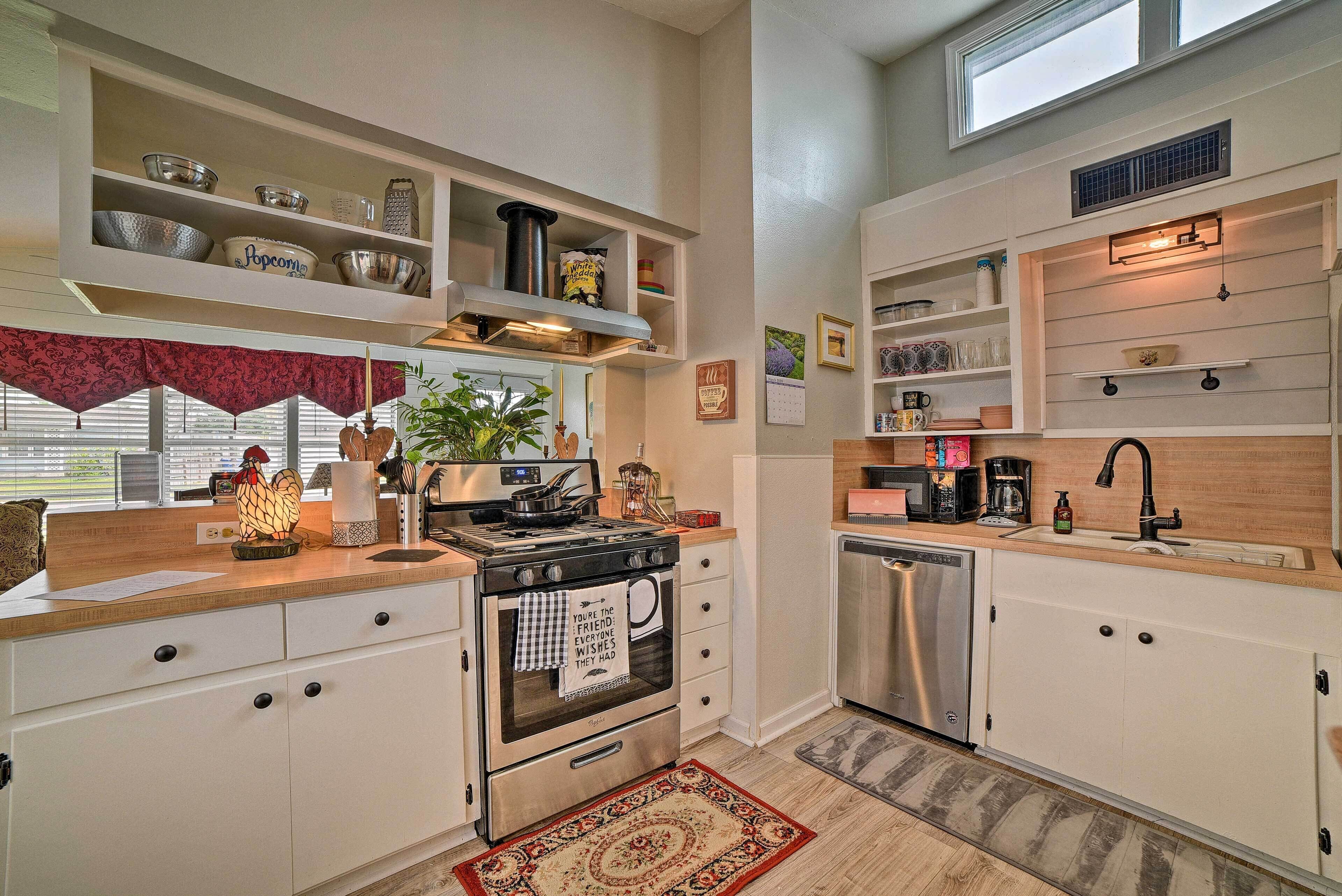 A modern kitchen with white cabinetry, a stainless steel stove, a dishwasher, and built-in shelves with kitchenware.