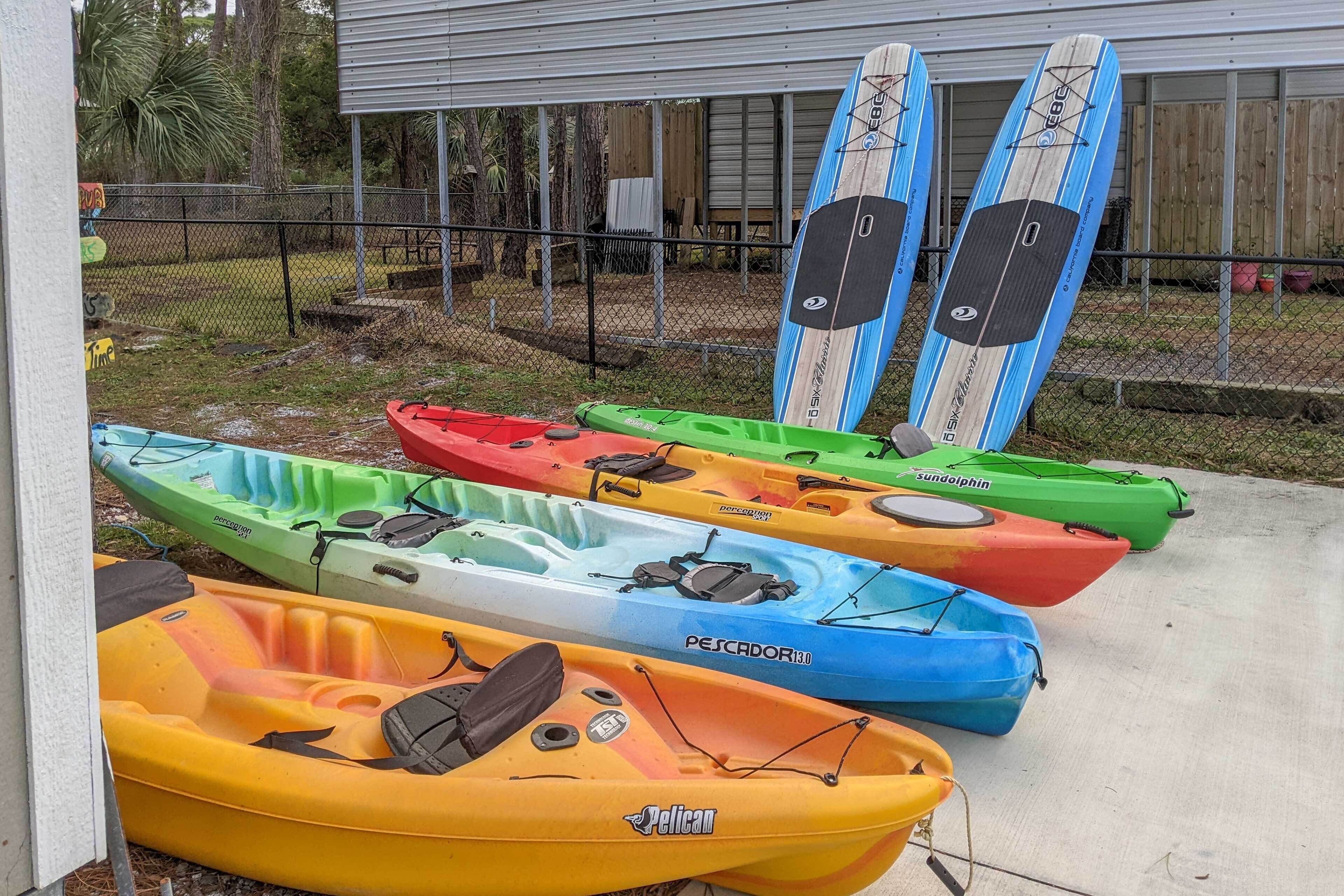 Una hilera de kayaks y tablas de remo de colores alineados frente a un edificio.