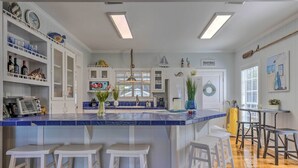 A kitchen with a blue-tiled island, white bar stools, and various decorative items. - Stunning Views & Waterfront Fun: Aloe Bay Home (Dauphin Island)