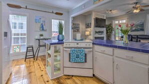 A kitchen with a white stove, blue-tiled countertop, and a window with blinds. - Stunning Views & Waterfront Fun: Aloe Bay Home (Dauphin Island)