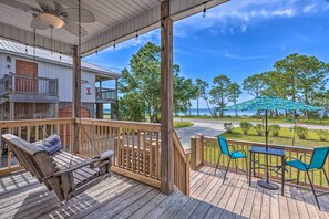 A wooden deck with a swing chair, a table with chairs, and a view of the beach and trees. - Stunning Views & Waterfront Fun: Aloe Bay Home (Dauphin Island)