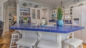 A kitchen with a blue tiled island, white cabinets, and a white refrigerator. - Stunning Views & Waterfront Fun: Aloe Bay Home (Dauphin Island)