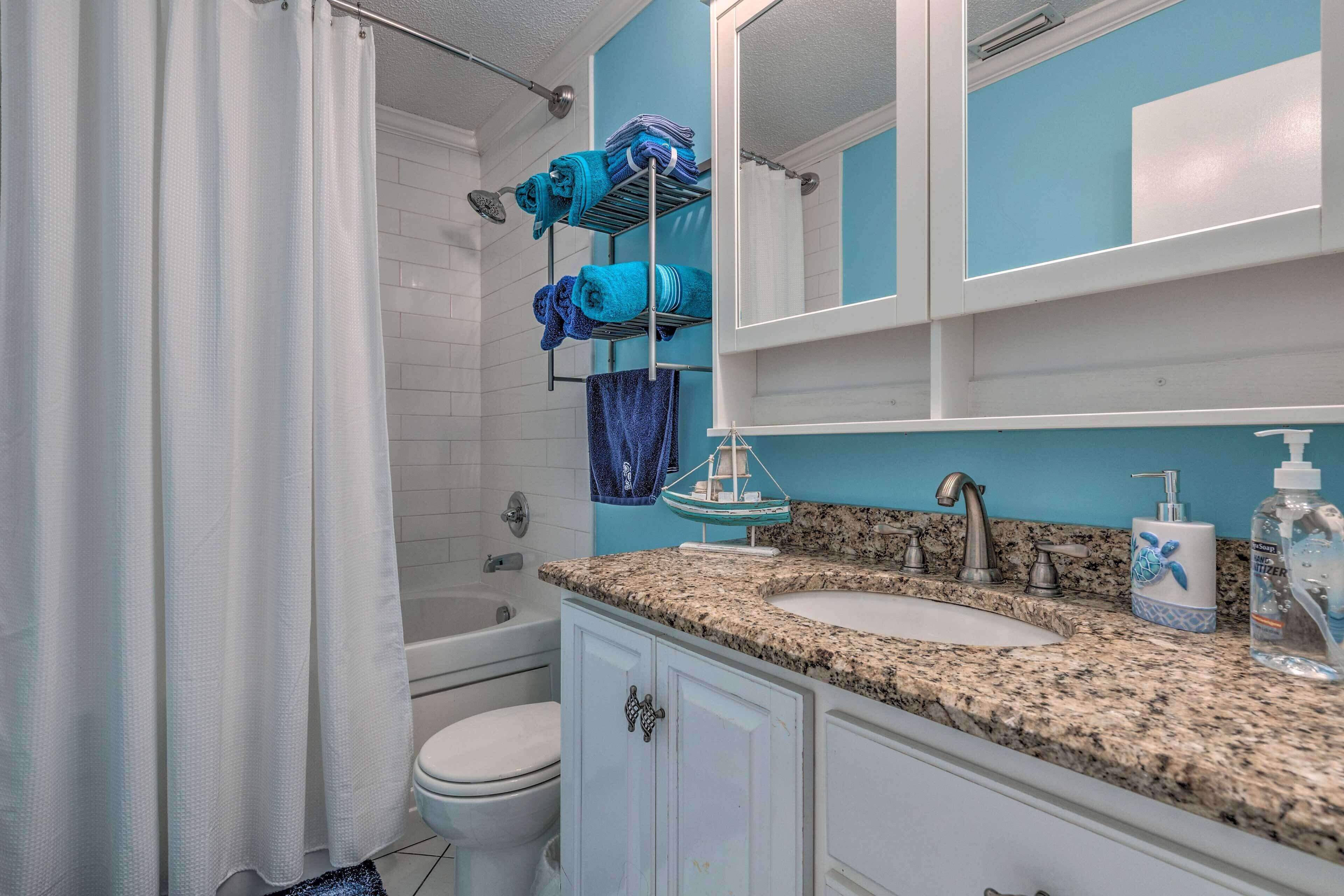 Un baño con inodoro blanco, lavamanos con encimera de granito y zona de ducha con cortina.
