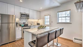A modern kitchen with stainless steel appliances, a herringbone backsplash, and a central island with bar stools.