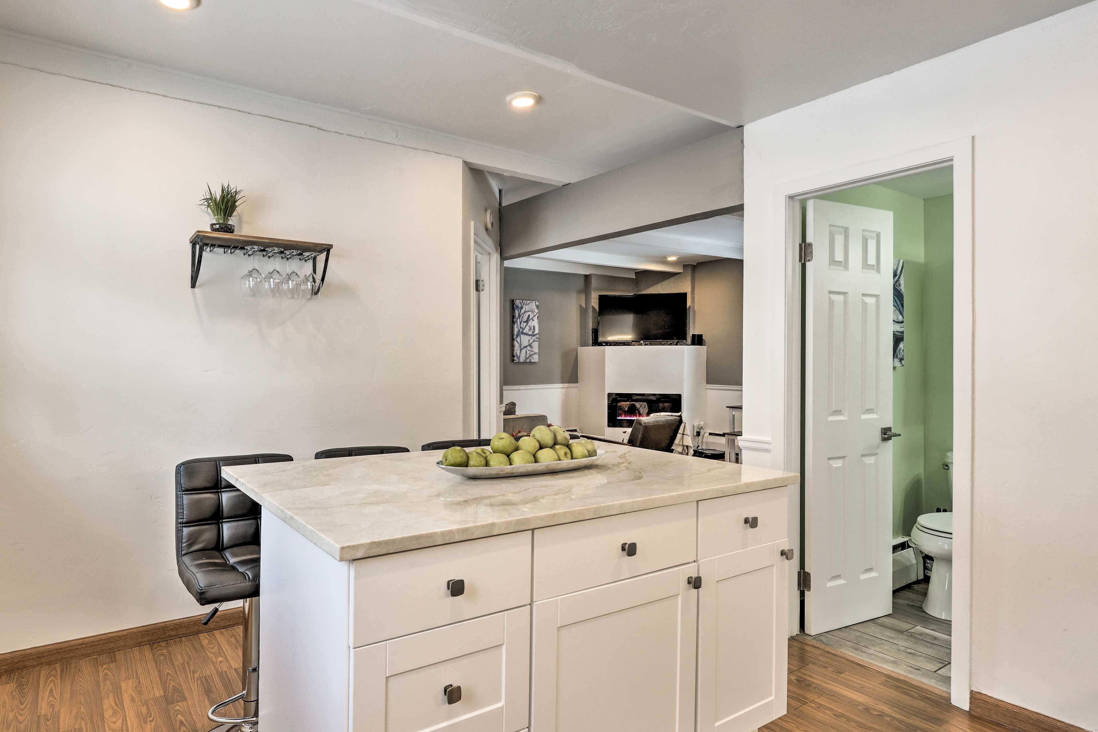 A modern kitchen with a marble countertop, a bowl of fruit, and a black leather chair.